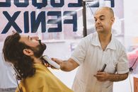 Barber expertly shaving a bearded client in a bustling barbershop.