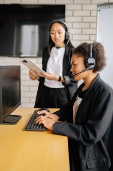 Two women in a call center wearing headsets, working at a computer.