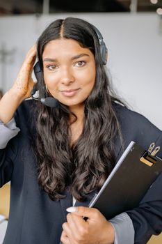 Young woman in professional attire using a headset, holding a clipboard