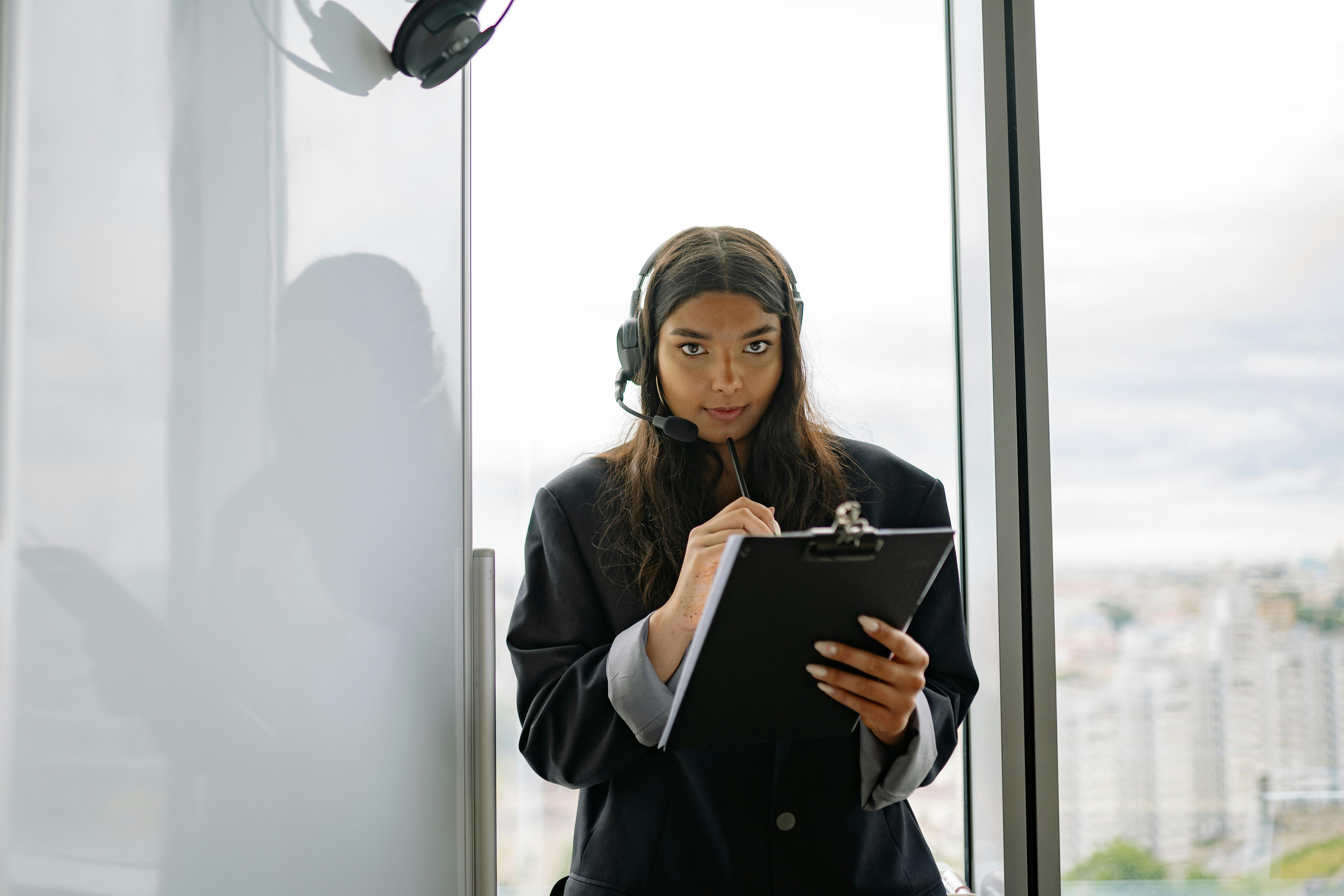 Confident woman in headset working with a clipboard in a modern office.