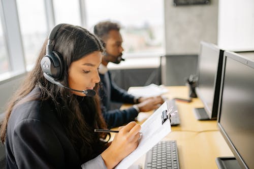 Free Woman With Headset Holding A Clipboard and Taking Notes Stock Photo