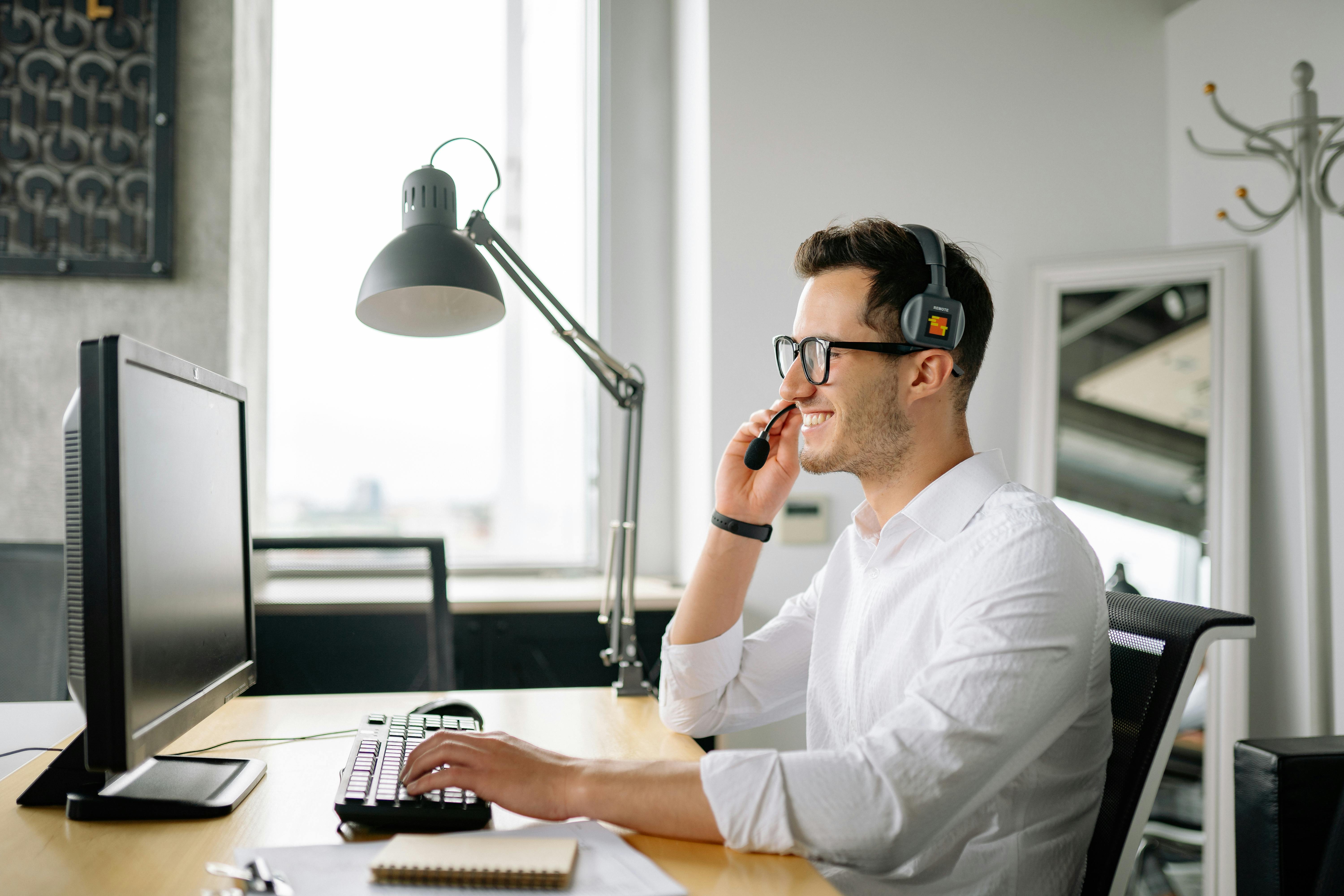 a smiling man wearing a headset looking at his computer screen