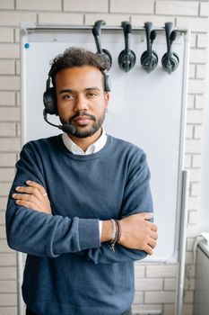 Serious call center agent with crossed arms, wearing a headset, standing by a whiteboard.