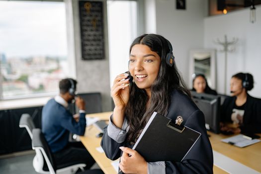 A smiling call center agent with headphones works in a modern office.