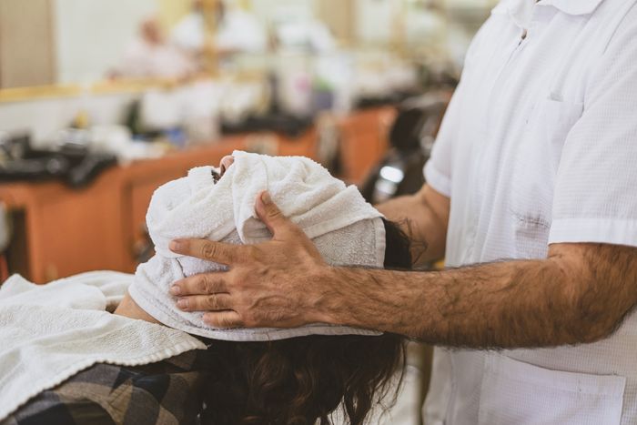 Barber pressing a warm towel over a client's face