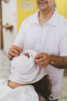 A barber performs a traditional grooming service by wrapping a towel over a client's face inside a barbershop.