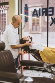 A professional barber shaving a customer's beard in a stylish barber shop setting.