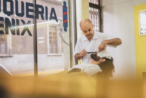 Free Barber performing a classic straight razor shave on a client in a bright barbershop. Stock Photo
