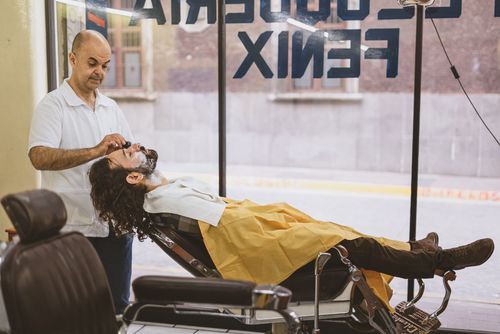 Free A barber skillfully shaves a client's beard as he relaxes in a barber chair inside a shop. Stock Photo