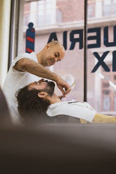 Barber expertly shaves a client's beard with a straight razor in a modern shop.