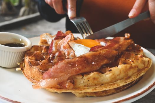 Delicious breakfast waffle topped with crispy bacon, sunny-side-up egg, and maple syrup.