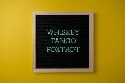 A letter board with 'Whiskey Tango Foxtrot' against a vibrant yellow background.