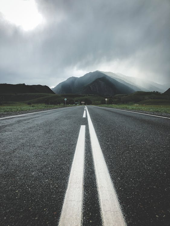 Empty Asphalt Road Under Gray Sky With Mountain View
