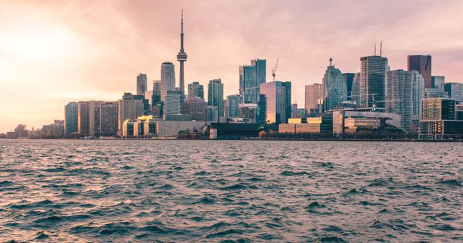 Panoramic view of Toronto's skyline with the iconic CN Tower during sunset, seen from across the water.