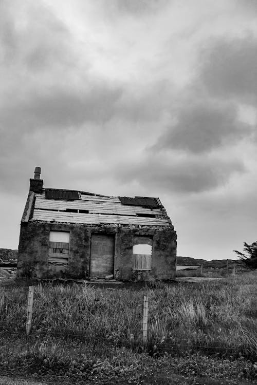 Grayscale Photo of an Abandoned House on Grass Field under the Cloudy Sky
