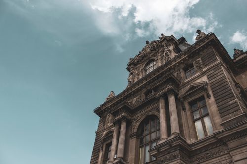 Free A majestic low-angle view of the historical facade of the Louvre Museum in Paris, showcasing its architectural grandeur. Stock Photo