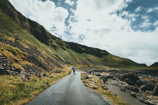 A scenic road through lush mountains with people walking in a picturesque natural setting.
