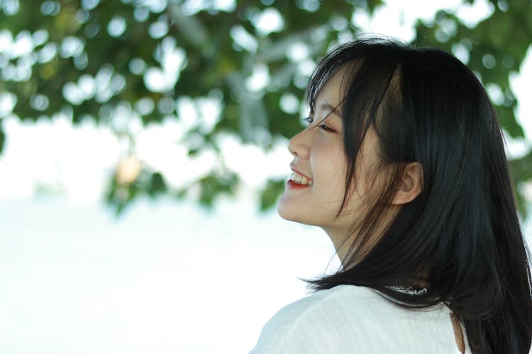 Profile Of A Smiling Woman With Black Hair Against Tree Leaves