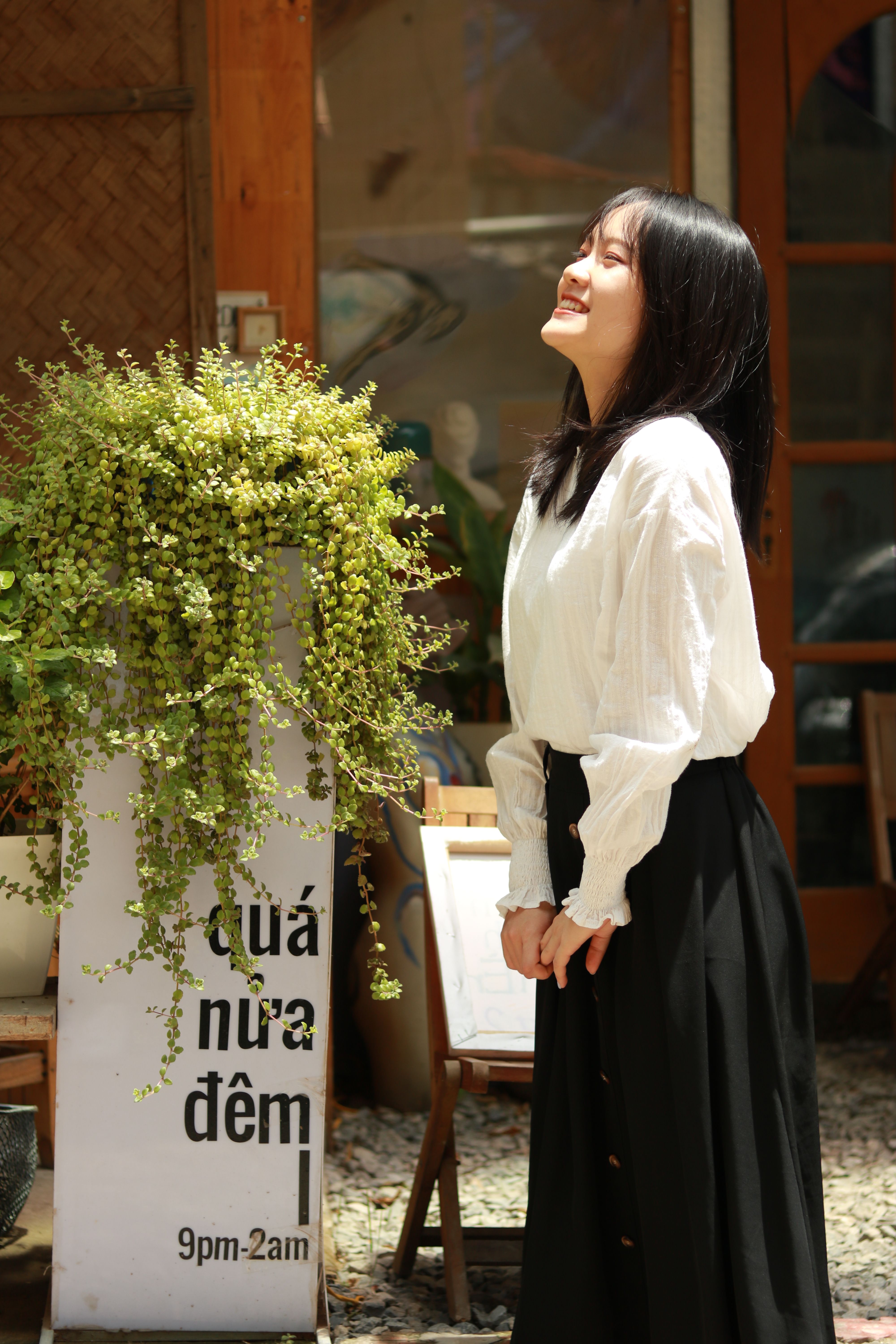 Happy woman soaking up the sun beside a lush plant in a stylish setting.