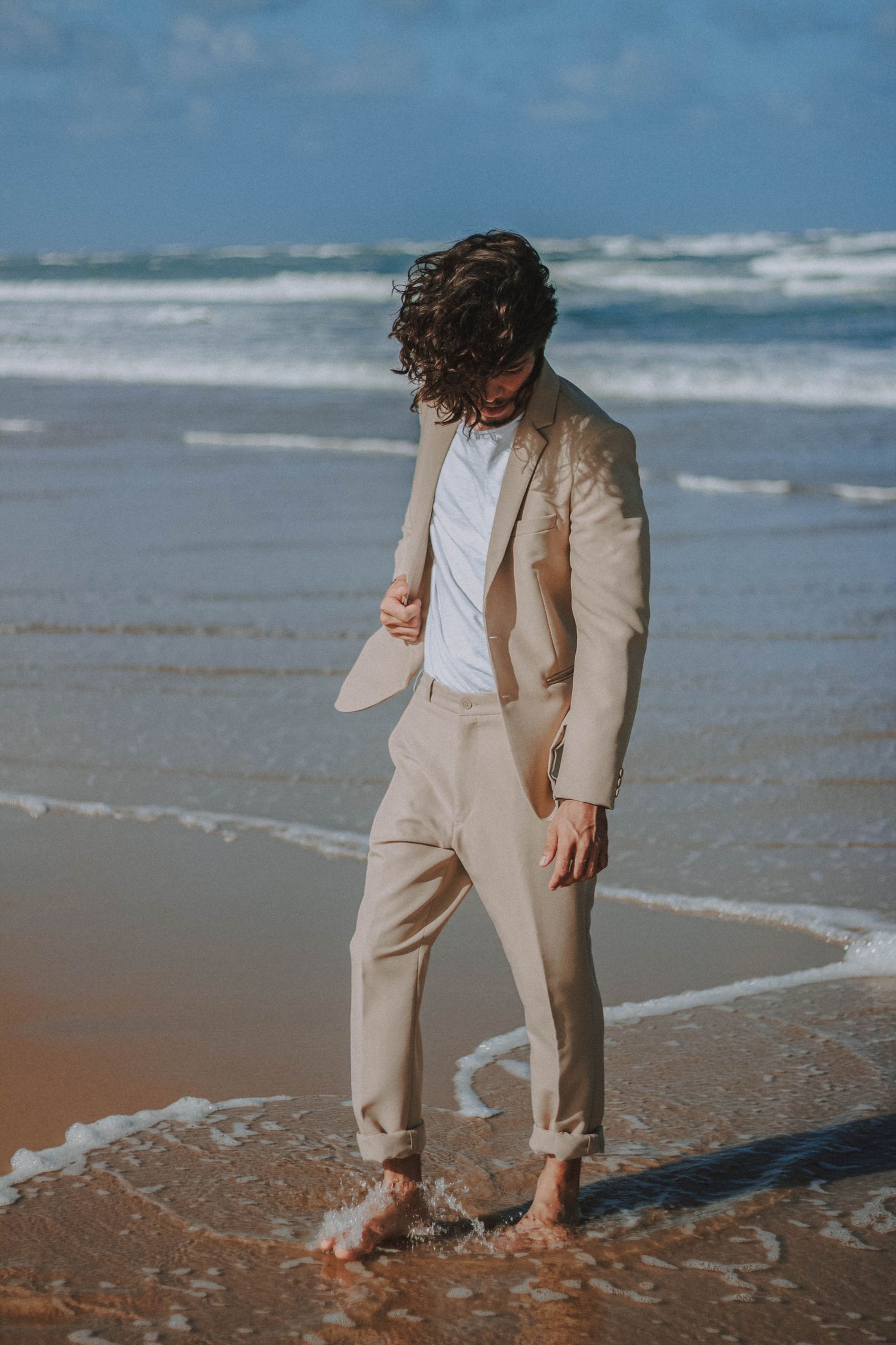 Hombre con traje beige de corte relajado paseando por la playa
