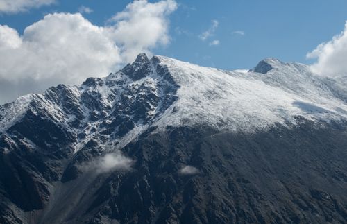 Free Scenic view of a snow-capped mountain peak with white clouds against a blue sky. Stock Photo