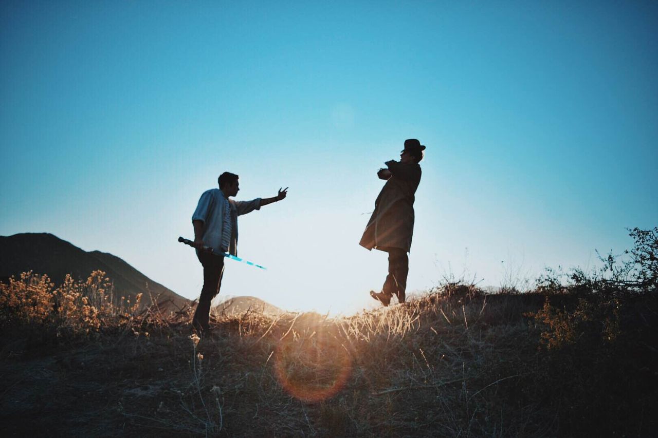 two men engage in a dramatic duel with swords silhouetted against a su