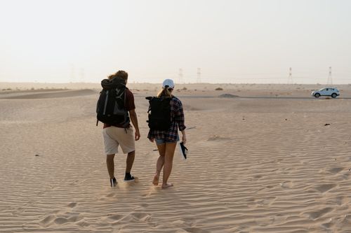 Free Two hikers walking through a vast desert landscape with a distant car and power lines. Stock Photo