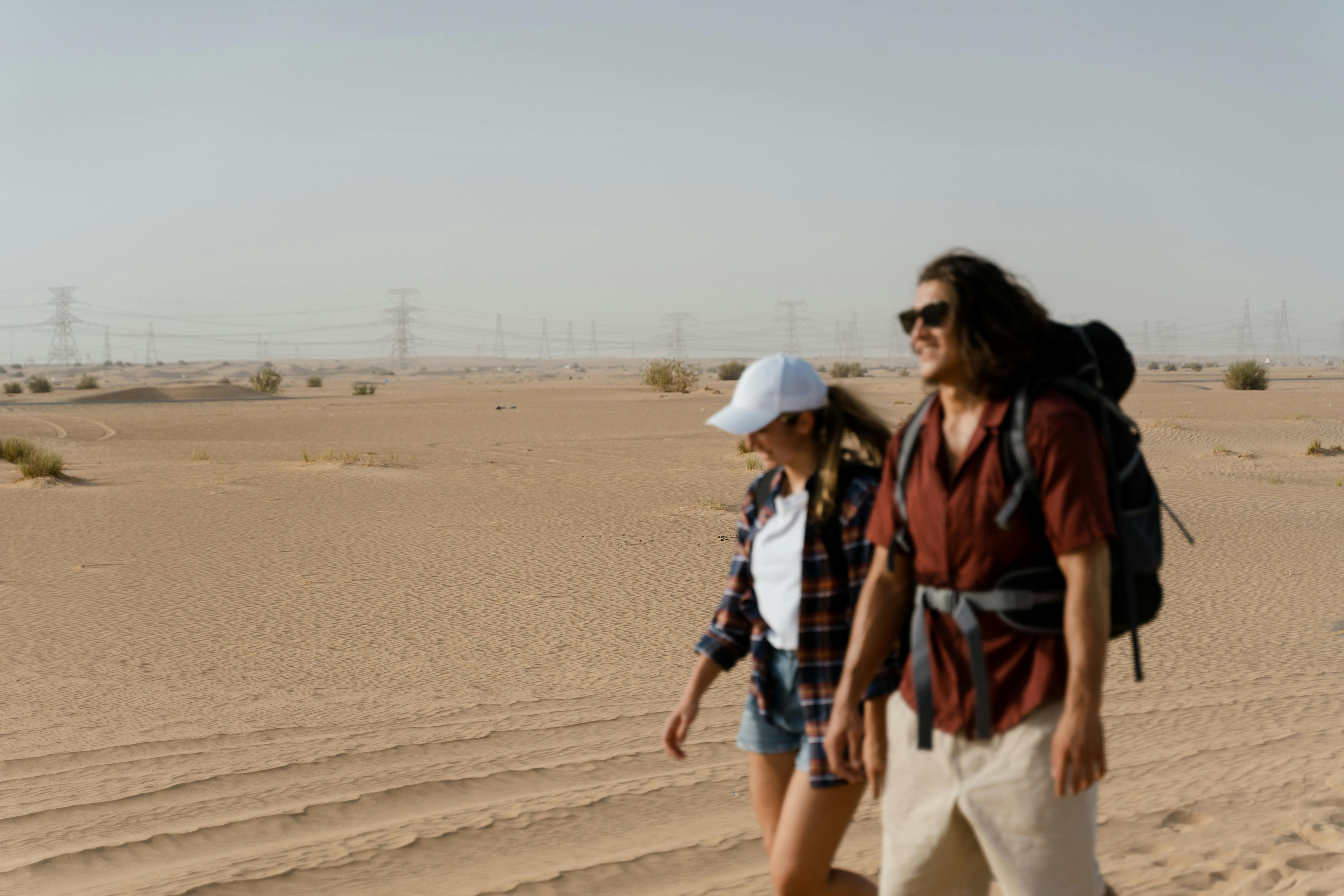 Two adults walking in a desert with backpacks, enjoying a warm sunny day.