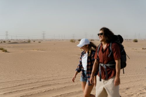 Free Two adults walking in a desert with backpacks, enjoying a warm sunny day. Stock Photo