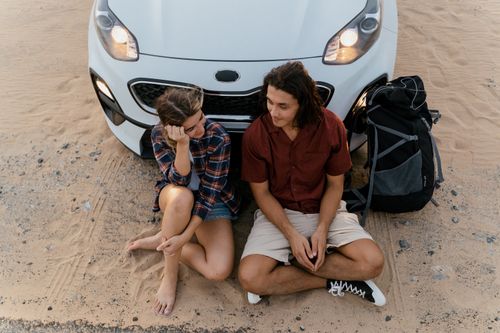 Free An adventurous couple sitting by a car in a sandy desert, perfect for travel themes. Stock Photo