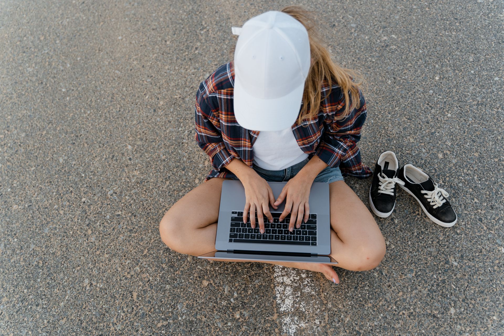 High-angle view of a woman working on a laptop while sitting on asphalt, embodying the digital nomad lifestyle.