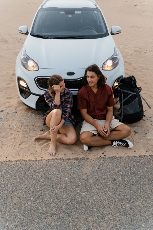 Free A couple sitting by their car in a desert, enjoying a peaceful moment together. Stock Photo
