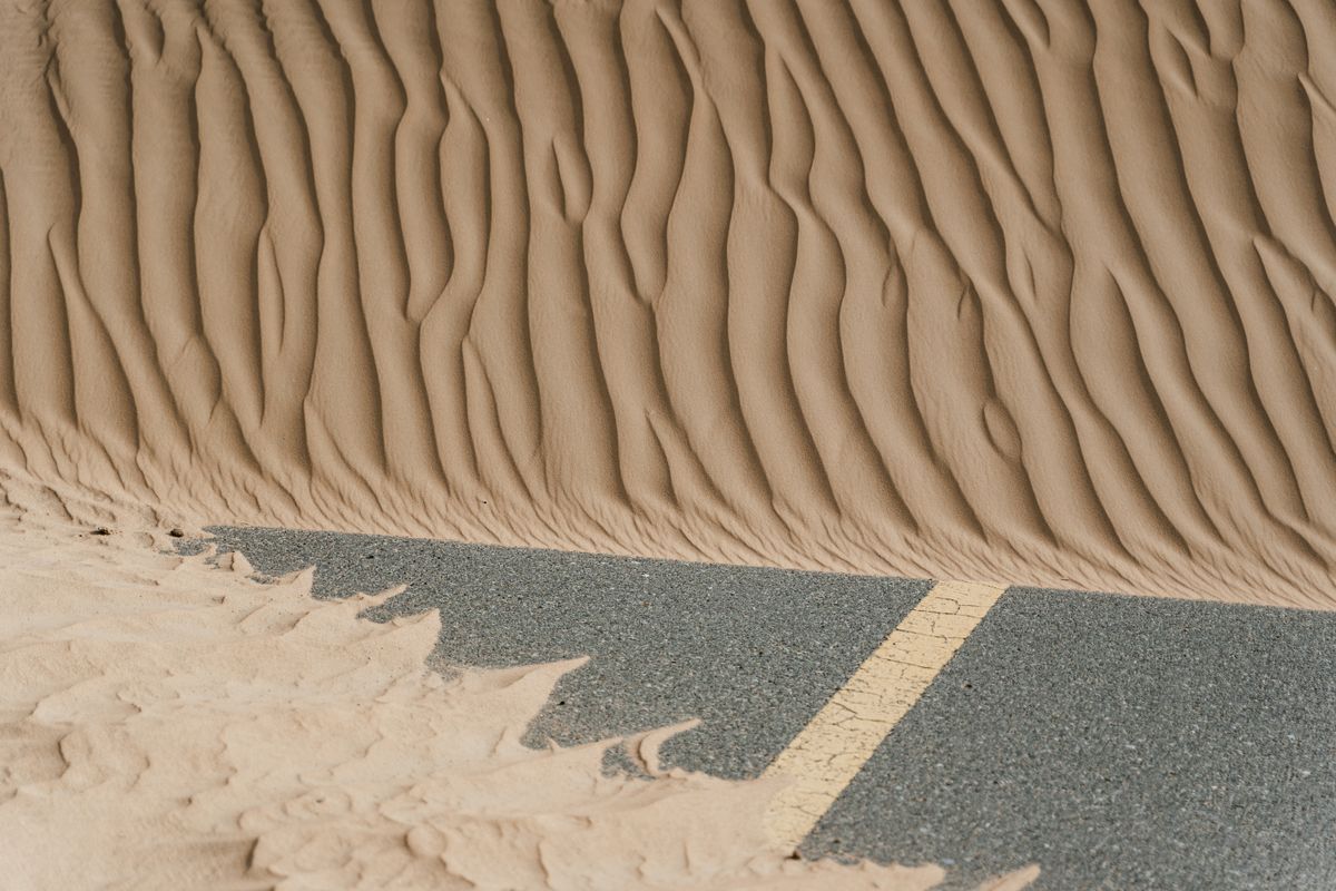 A road disappearing under desert sand dunes — photo by MART PRODUCTION on Pexels