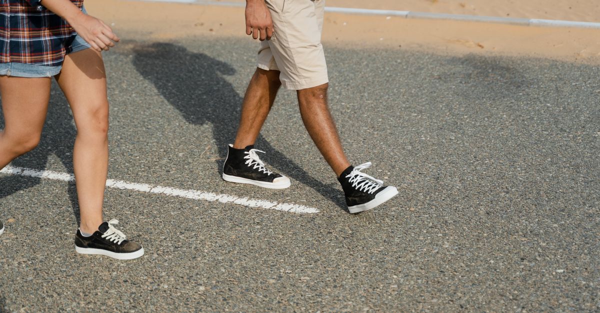 Close-up of two people in sneakers walking down a desert road.