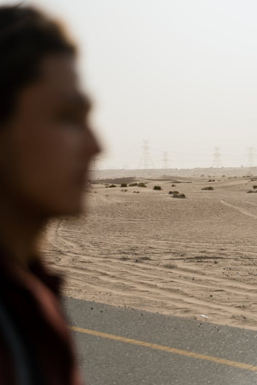 Free Blurry Photo of a Person Standing Near the Asphalt Road in the Desert Stock Photo