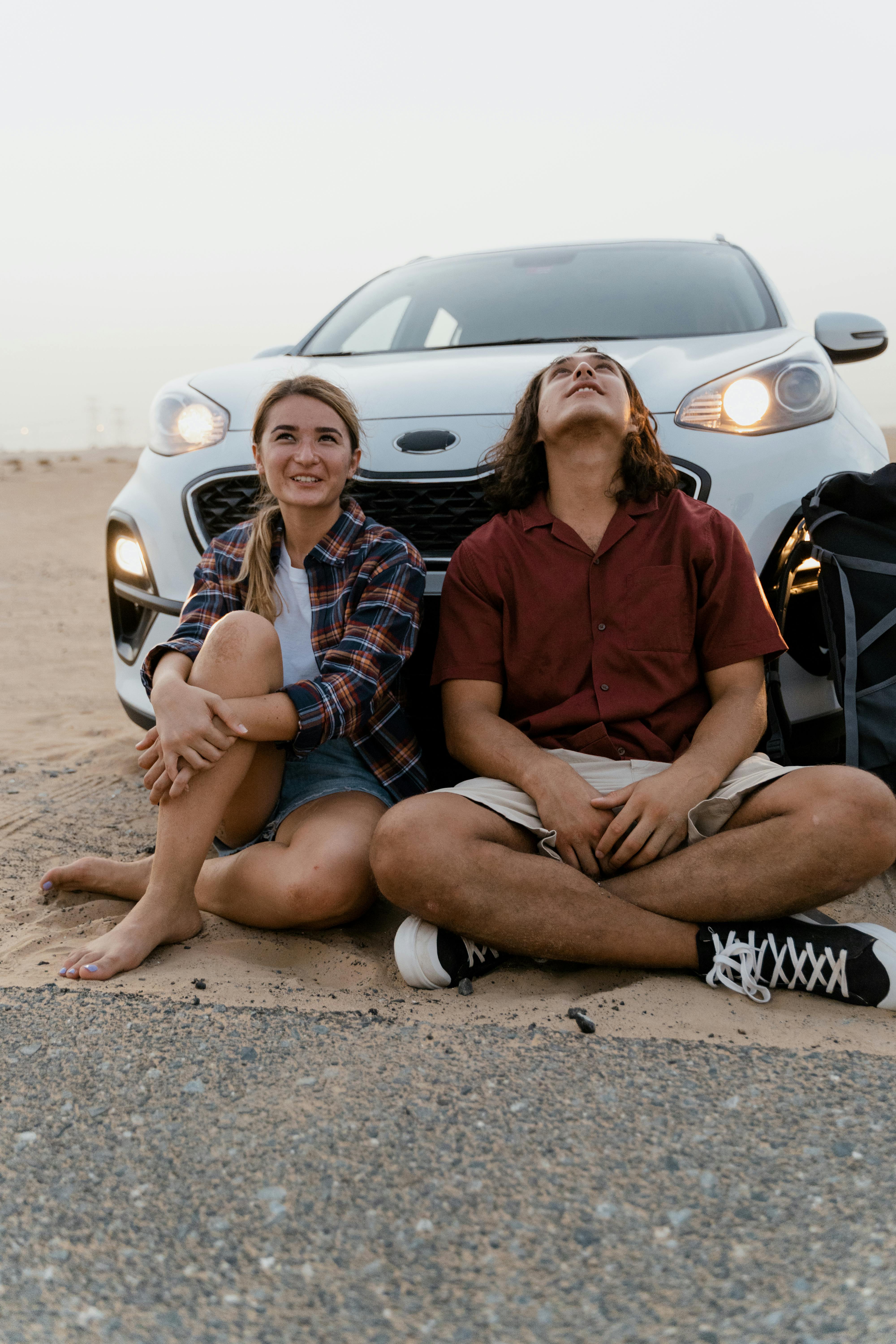 couple sitting on the ground in front of a car