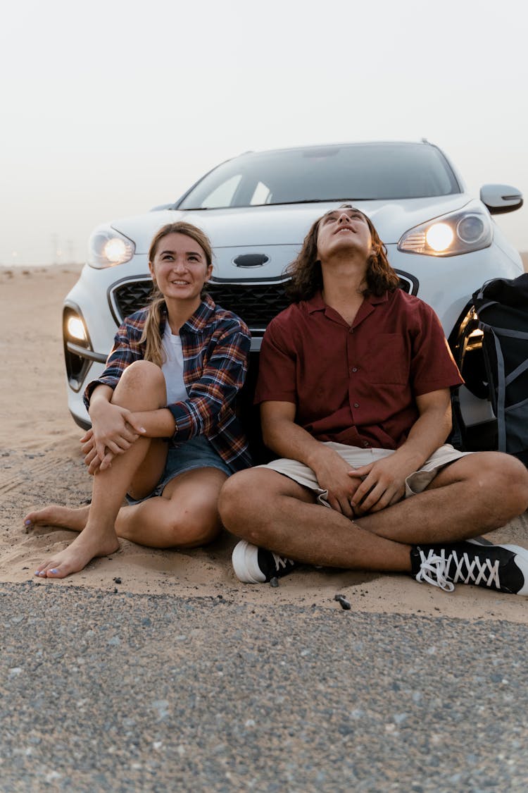 Couple Sitting On The Ground In Front Of A Car