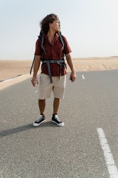Young man with backpack on a deserted road in the desert, exploring and adventuring.