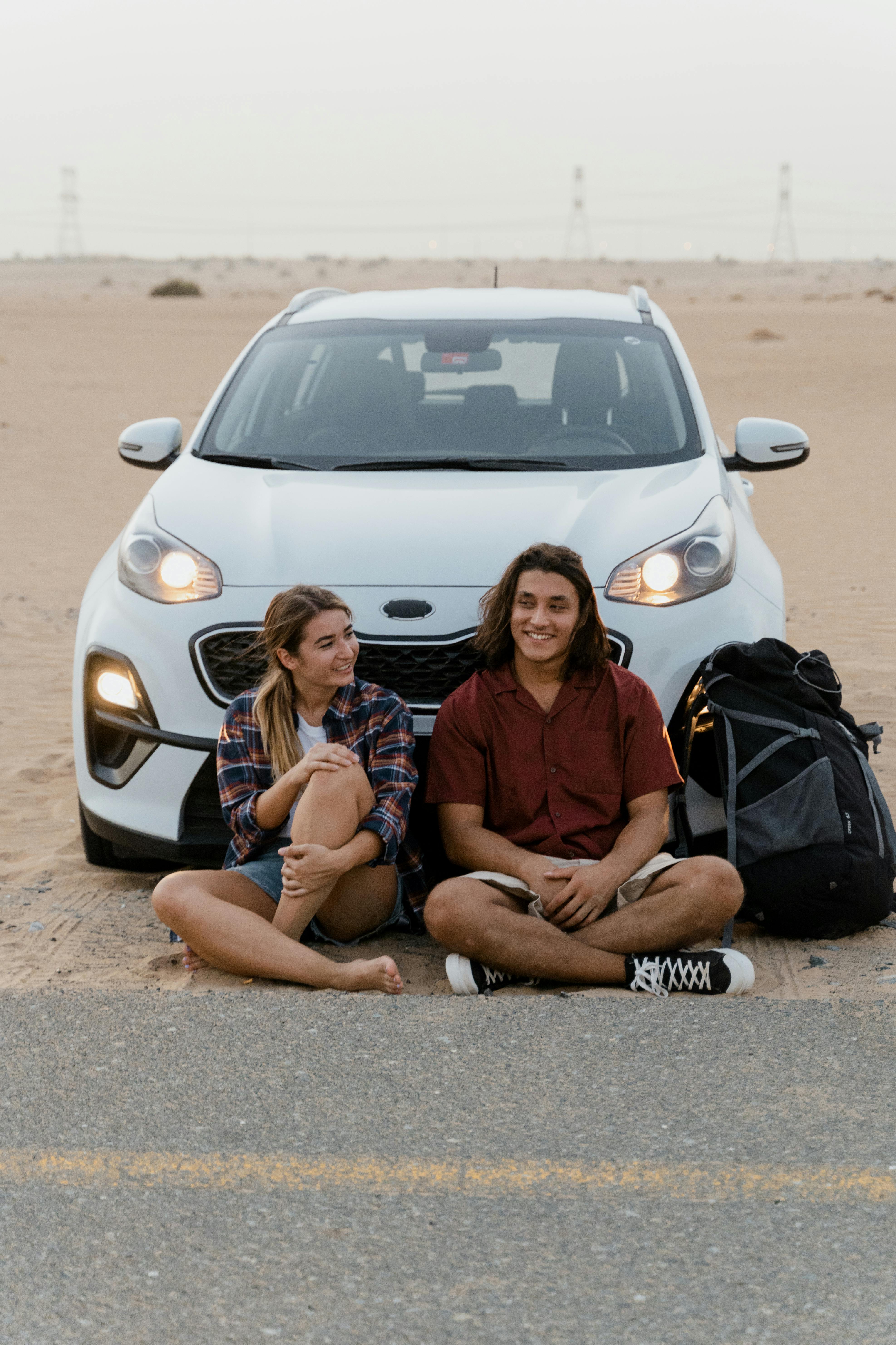 man and woman sitting on the road in front of a car