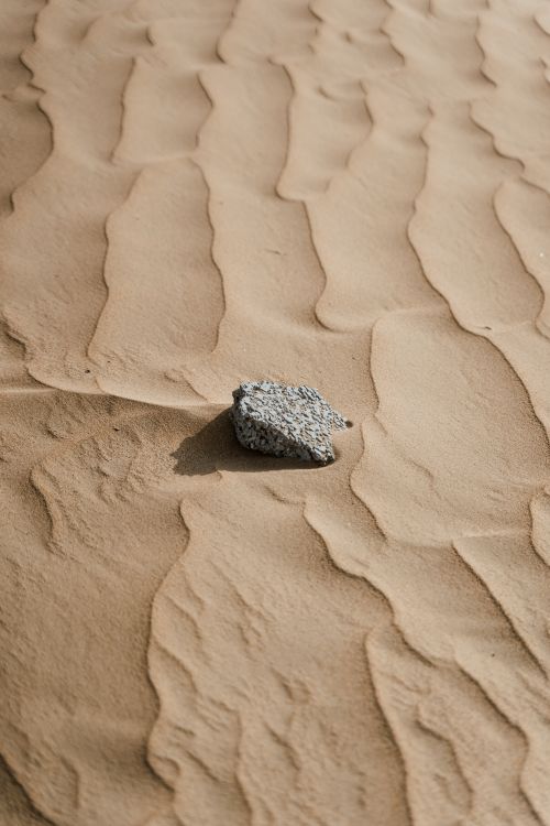 Free Minimalist desert shot featuring a lone rock on rippled sand dunes. Stock Photo