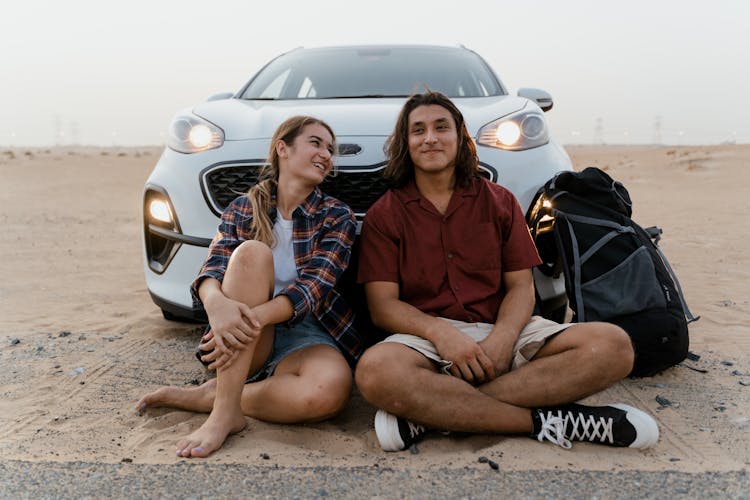 A Couple Sitting In Front Of Their Parked Car On A Desert