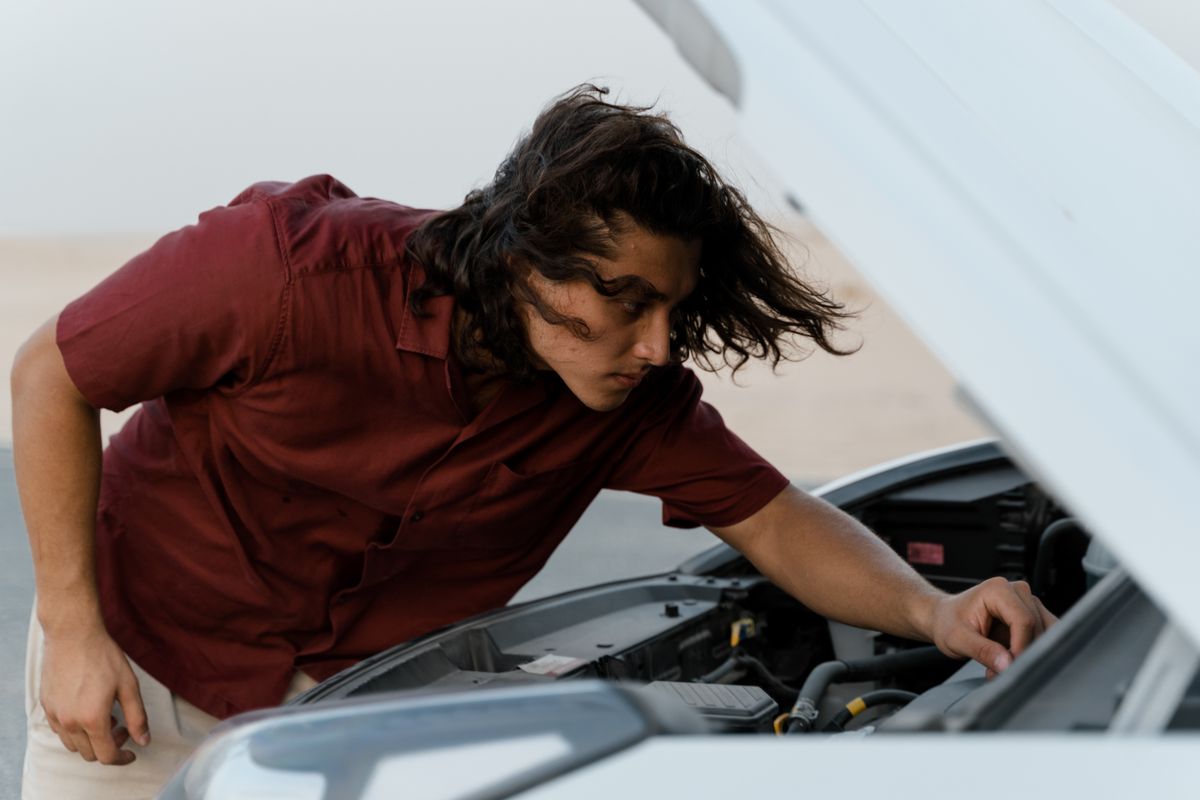 Person checking under the hood of a car outdoors