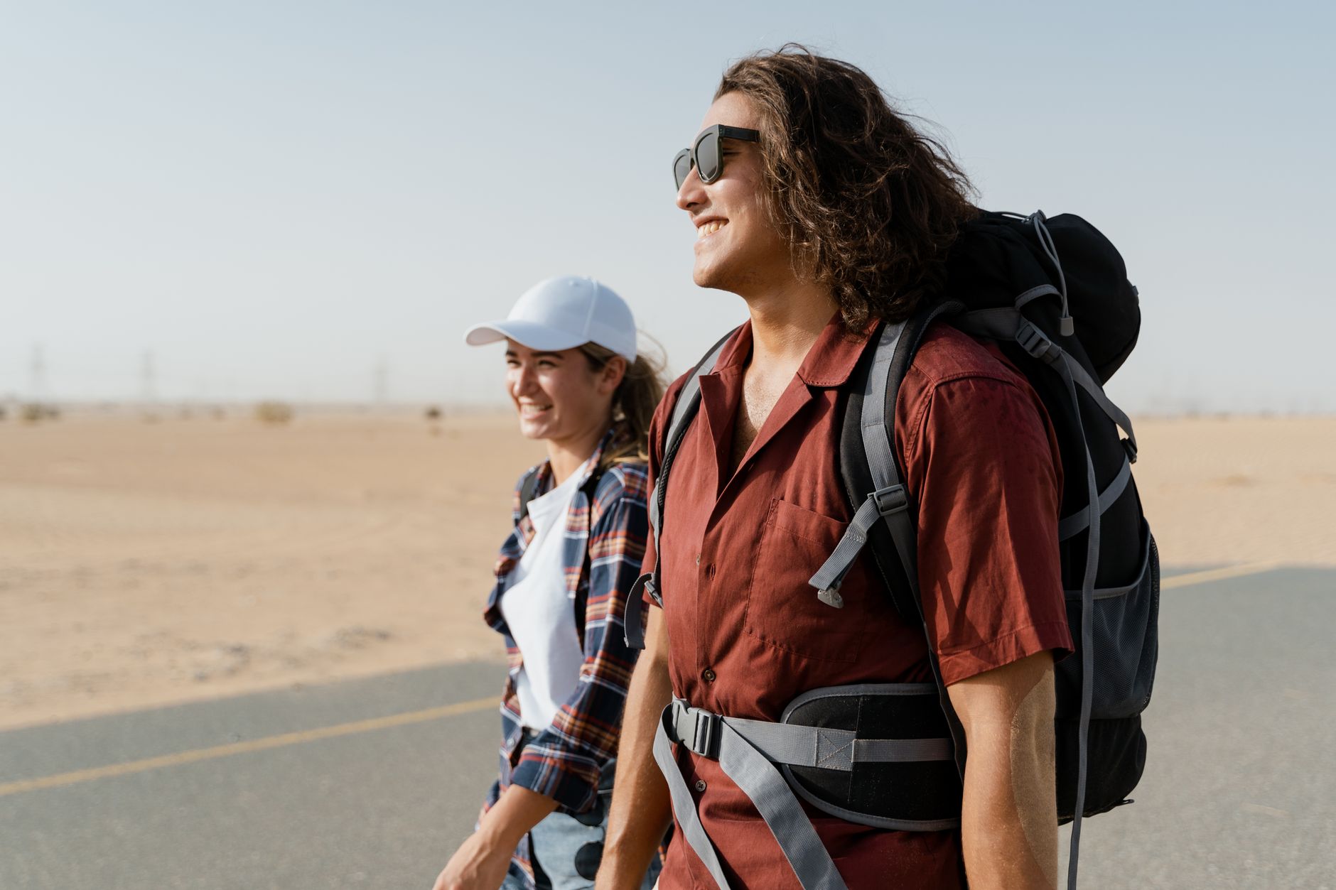 A smiling young couple hikes on a desert road, embodying happiness and adventure.