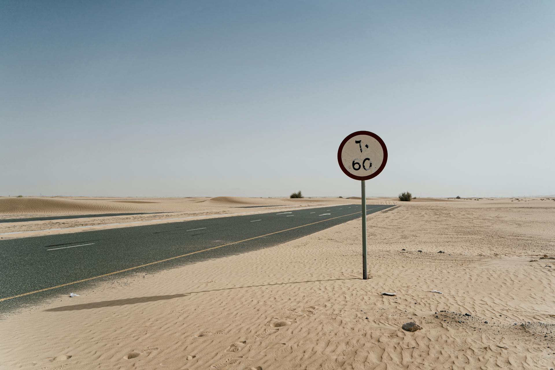 Desert road with speed limit sign, under clear blue sky, serene and empty.