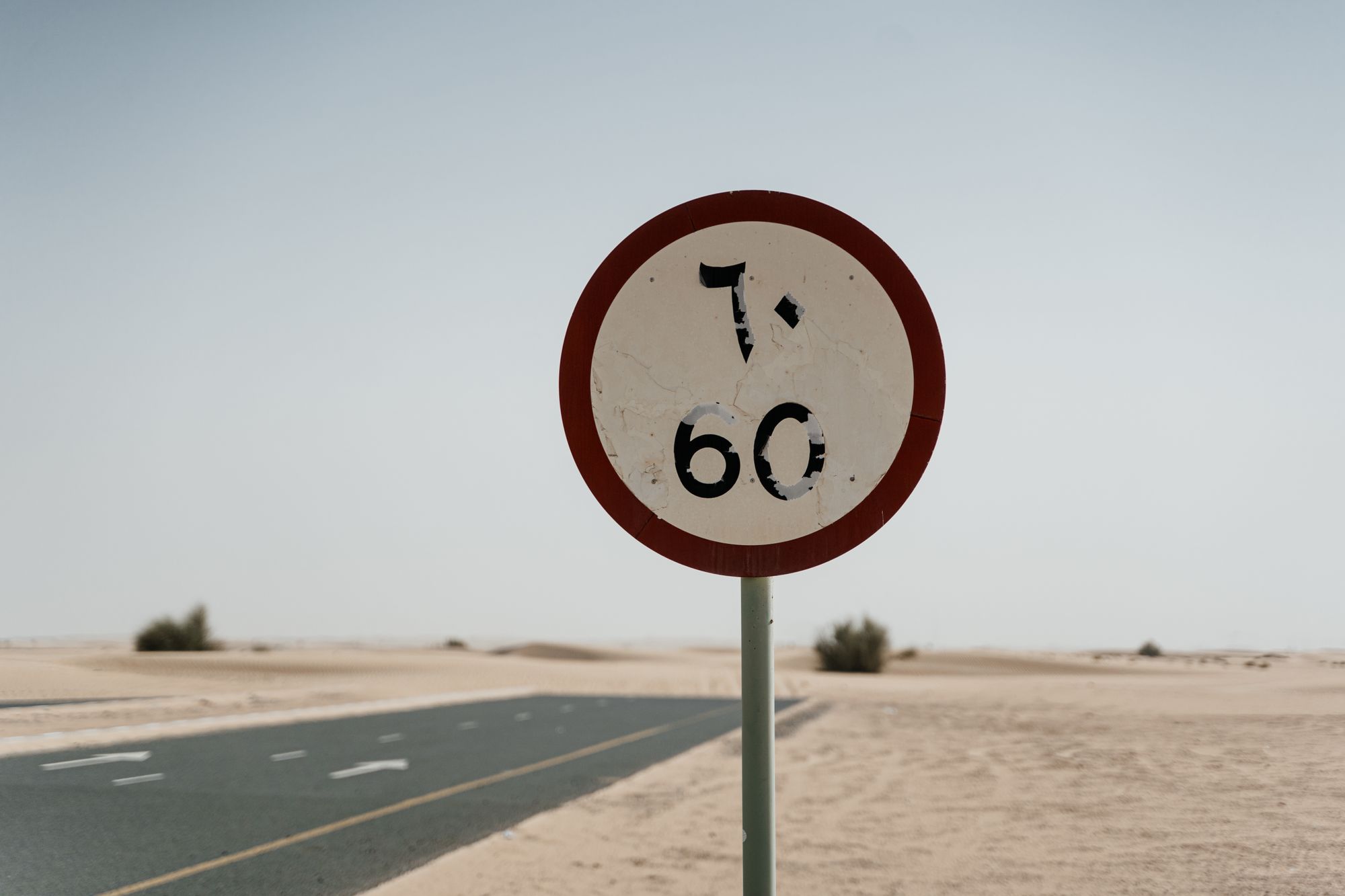 Carretera de dos carriles en zona desértica bajo sol intenso, con distorsión de calor sobre el asfalto