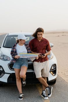 Couple leaning on a white car reading a map in a desert setting.