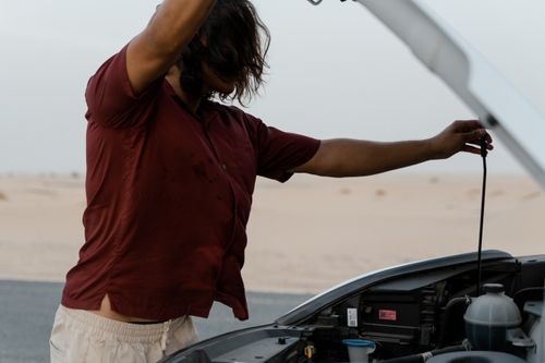 Free A man examines the engine of a car on a deserted road, highlighting automotive maintenance. Stock Photo