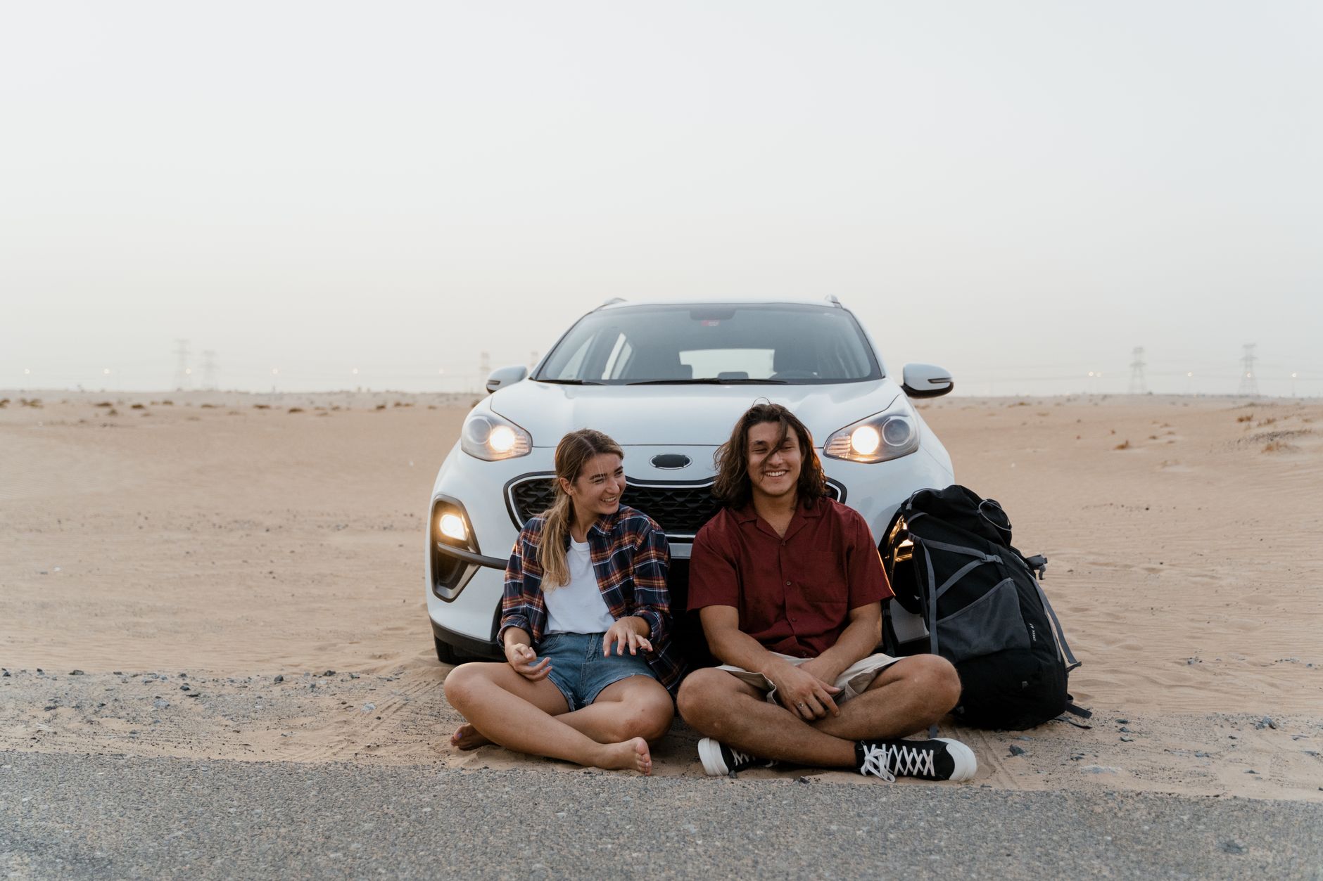 Young travelers relaxing by their car in the desert, enjoying a scenic road trip adventure.