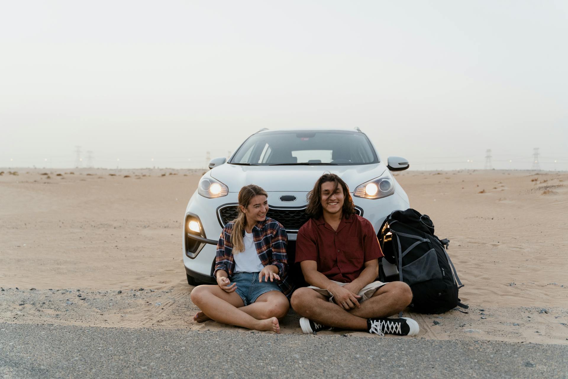 Young travelers relaxing by their car in the desert, enjoying a scenic road trip adventure.