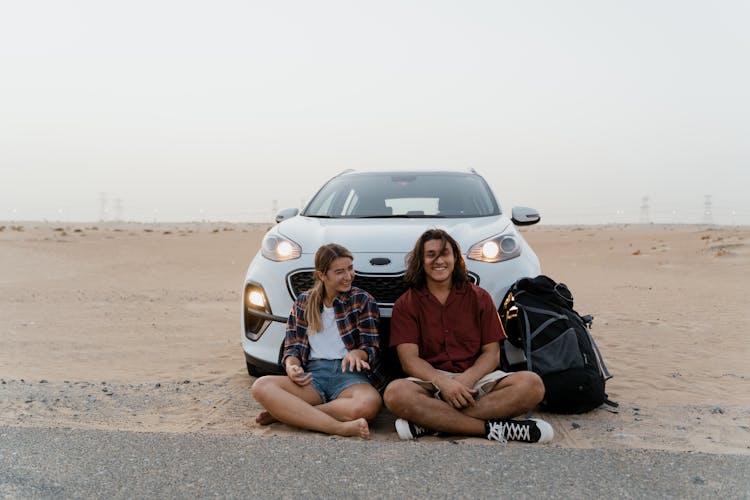 Couple Sitting In Front Of Their Car In The Desert